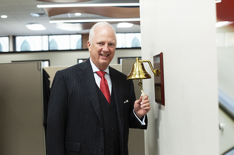 tony caldwell standing in a hallway ringing a gold bell