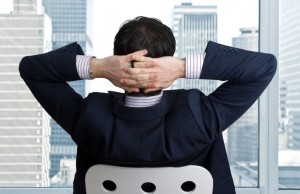 A man relaxing with his hands behind his head taking in the city view after a successful business day.