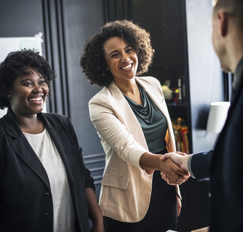 2 women, one shaking hands with a man, all in business attire