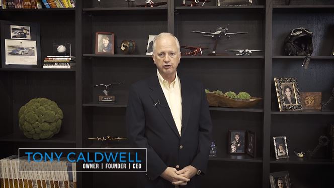 still shot of tony standing in front of a bookshelf with various trinkets